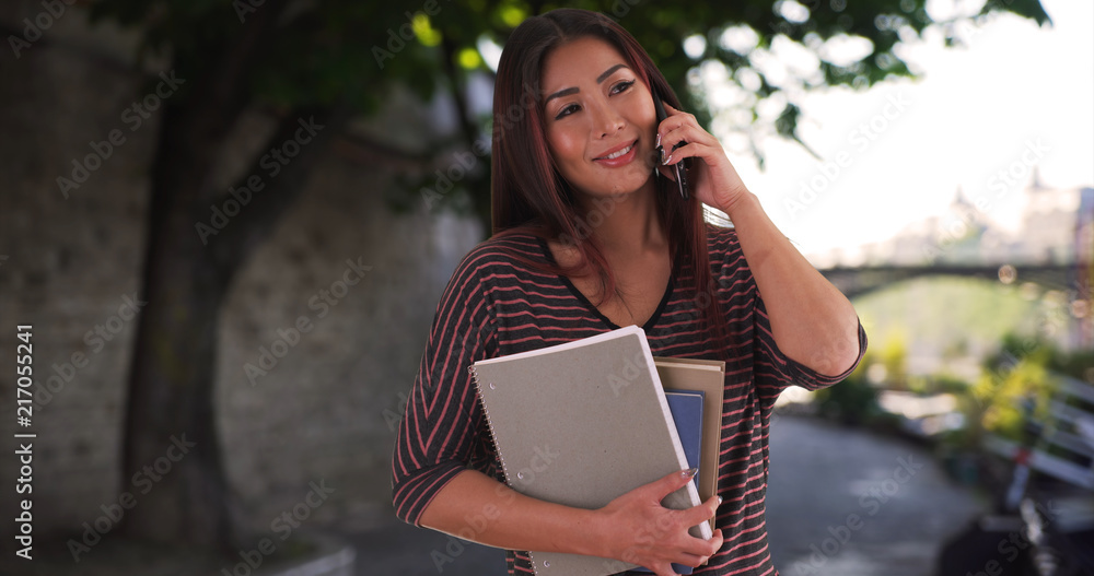 Naklejka premium Cute Asian female studying in Europe chats happily on mobile phone