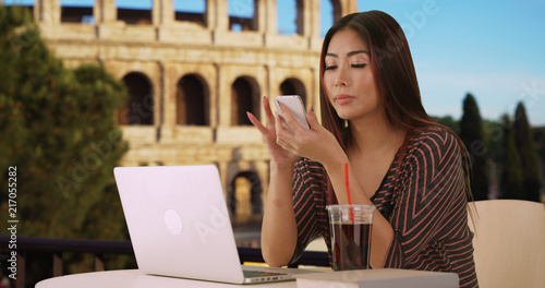 Photography Cute Asian female talks to friend on phone while typing on laptop near Coliseum