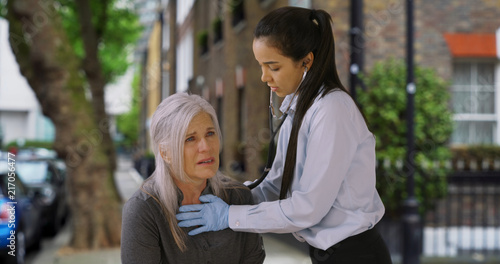 Latin woman paramedic listens to senior woman breathing on the street