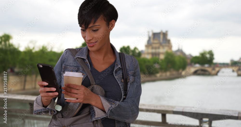 Obraz premium African-American beauty in Paris checking smartphone and drinking coffee