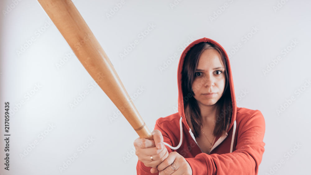 Girl athlete with a baseball bat in a red hoodie. Girl or criminal woman, holding baseball bat in hand on white background. Body art. Sport and training