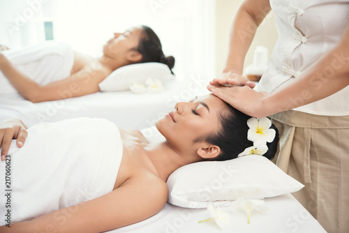 two Beautiful young woman getting spa massage salon and white flower on her ear.