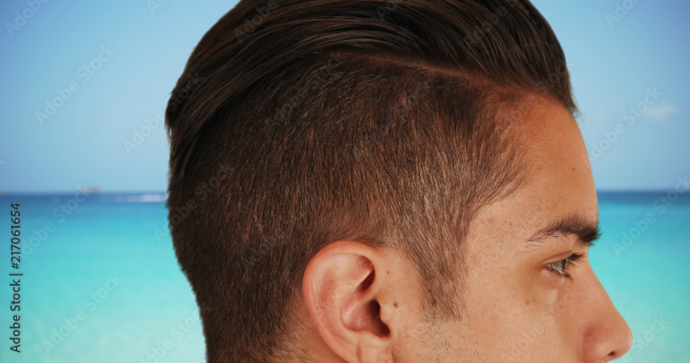 Close up of handsome Latin male with cool undercut standing by ocean Close up of handsome Latin male with cool undercut standing by ocean