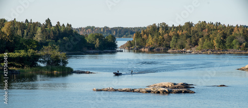 Summer vacation idyll in Sweden - A panorama view of Stockhol archipellago showing the sea, small islands and a motor boat towing a person on water skis.