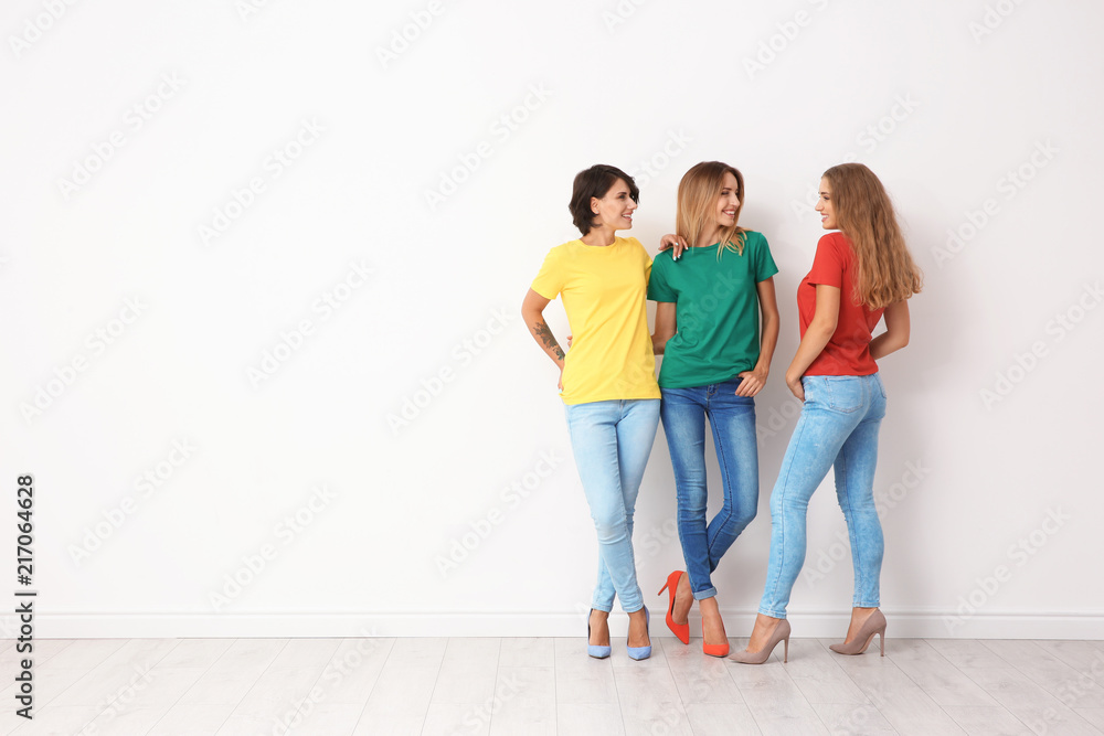 Group of young women in jeans and colorful t-shirts near light wall Group of young women in jeans and colorful t-shirts near light wall