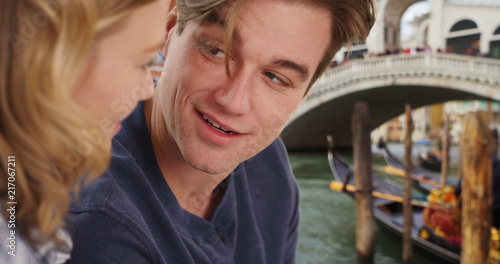 Side view of happy millennial couple in Venice talking near Italian bridge