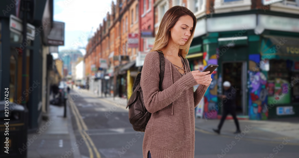 Young female walking through hipster neighborhood using cellphone