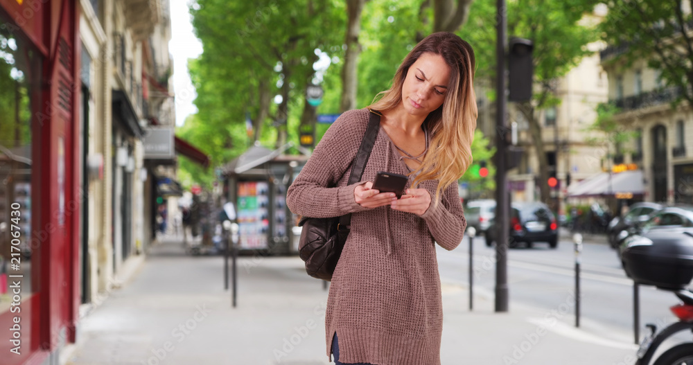 Pretty Caucasian woman walks down the street using smartphone for directions