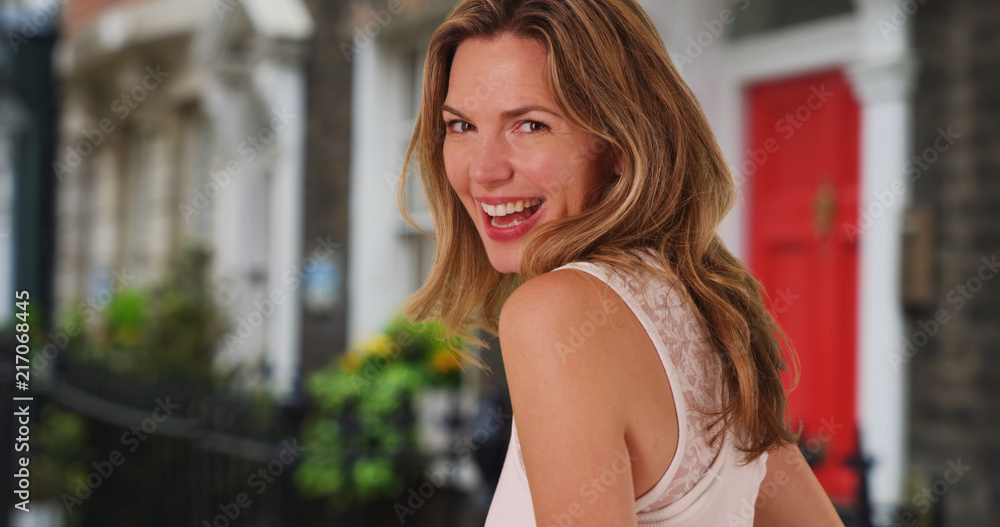 Pretty Caucasian woman smiling in front of residential home