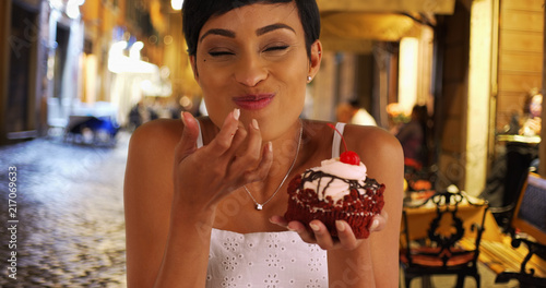 Foto Black woman takes messy bite of huge red velvet cupcake