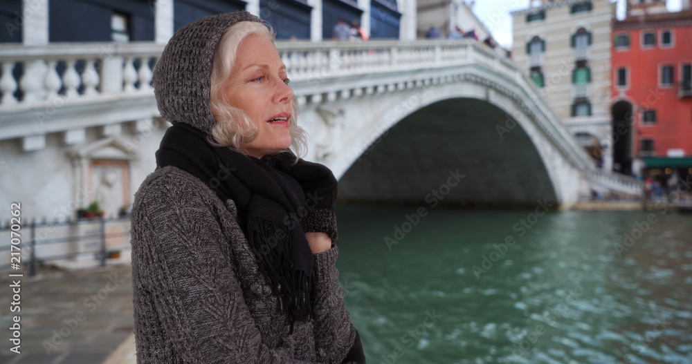 Obraz premium Mature woman in sweater and scarf looking out over canal on venice vacation