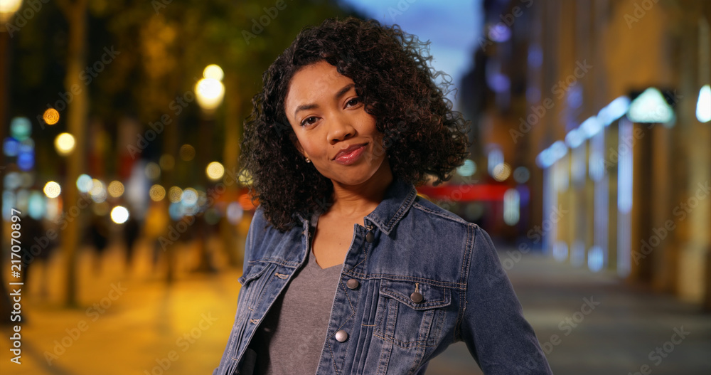 Happy African American woman in denim jacket smiling on city street at night