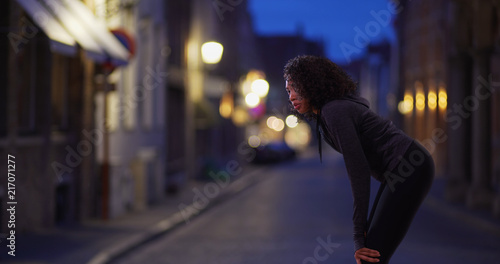 Black woman athlete in the city at night catching her breath
