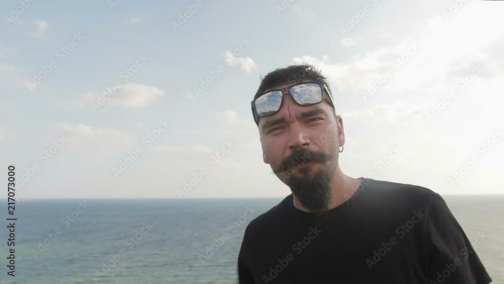 Dude beatnik twirl his mustache, he's wearing sunglasses and a black t-shirt on a blue sea background Dude beatnik twirl his mustache, he's wearing sunglasses and a black t-shirt on a blue sea background