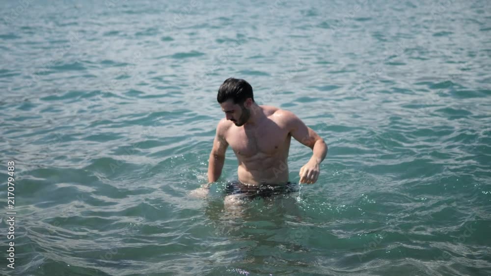 Handsome muscular young man standing in the sea by the coast and the beach Handsome muscular young man standing in the sea by the coast and the beach