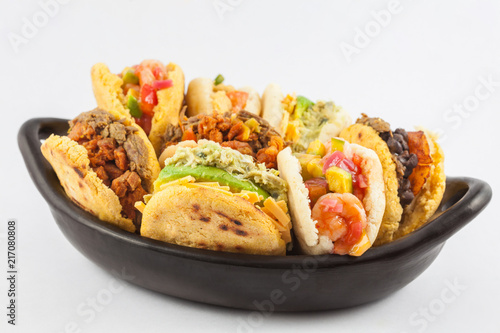 Arepas with assorted fillings served in a black ceramic dish on white background