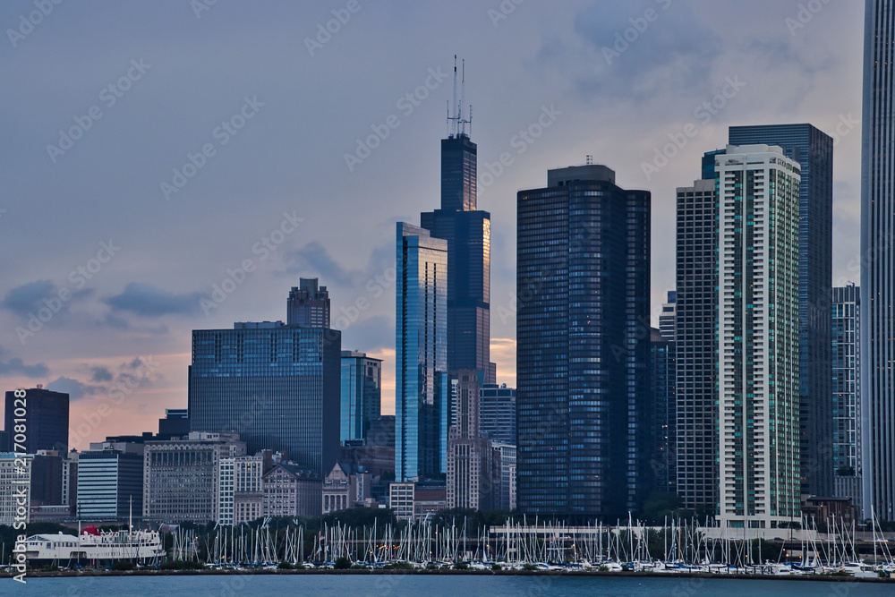 Sunset reflecting off of skyscrapers, with view of sailboats in a Lake Michigan marina in foreground, along Lake Michigan's lakefront in downtown Chicago.