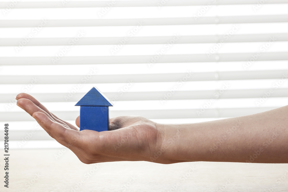 Naklejka premium woman hand hold a blue wood house at the office.