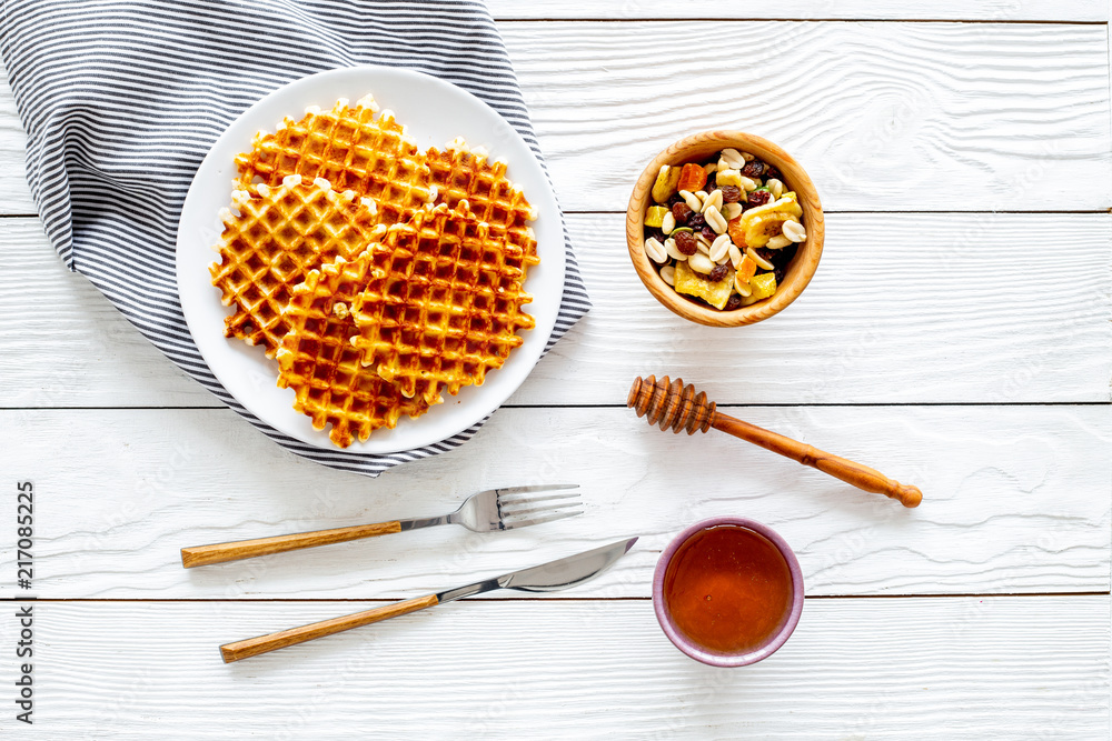 Traditional belgian waffles near dried fruit, nuts and honey on served table with tablecloth on white wooden background top view copy space Traditional belgian waffles near dried fruit, nuts and honey on served table with tablecloth on white wooden background top view copy space