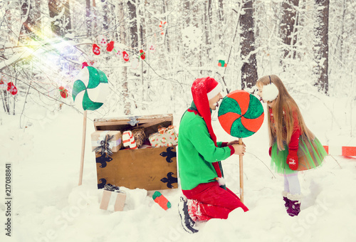 father and little daughter walk in costumes of flowers traditional for elves Santa's helpers in the winter forest under the snow with a chest of gifts and giant candy new year