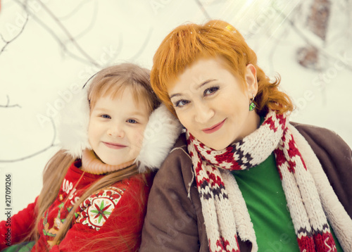 mom and daughter, both red hair walking in costumes of flowers traditional elves Santa's helpers in the winter forest under the snow with a chest of gifts and giant candy