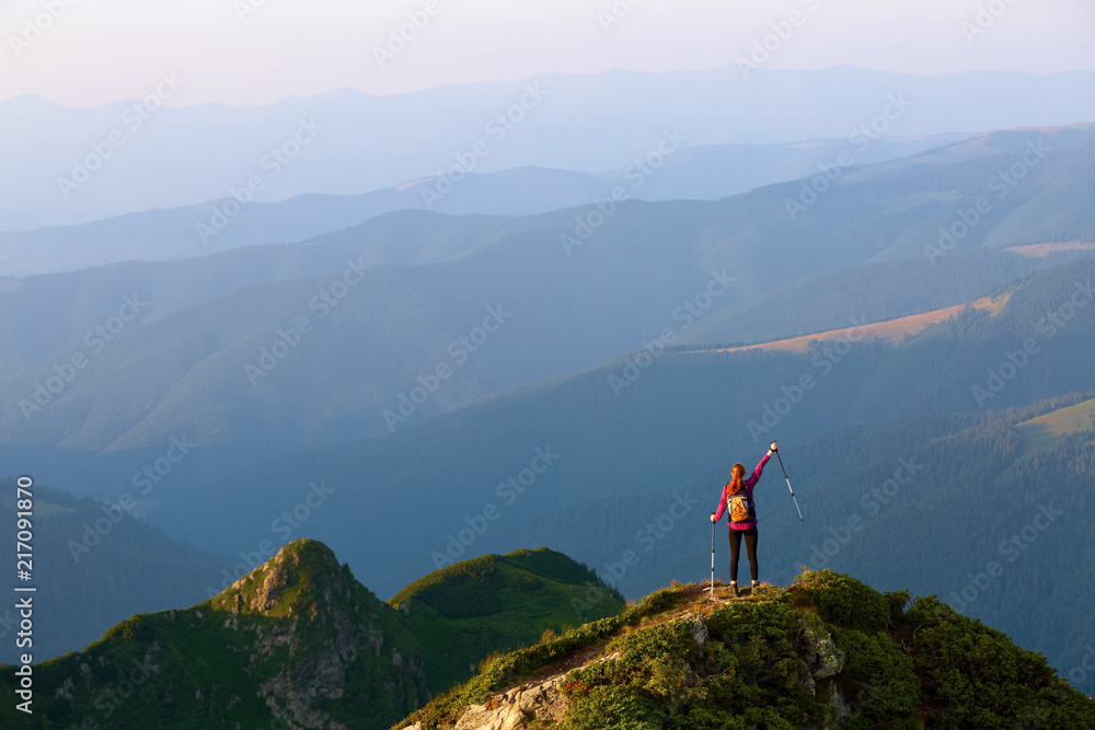 On the edge of the abyss on the lawn among the landscapes with high mountains and fields there is a tourist with a backpack and trekking sticks, and indicates the path.