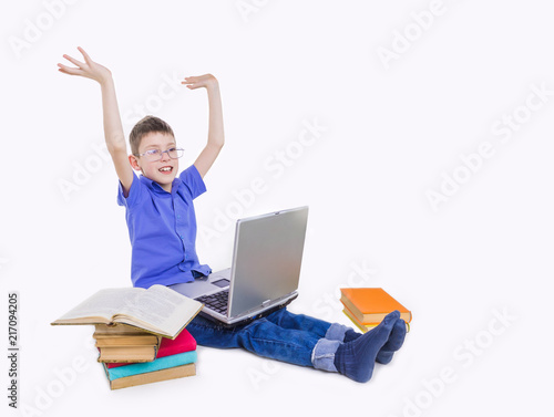 Portrait of cute teen schoolboy sitting near books and typing on laptop keyboard. Happy and surprised little boy, caucasian model isolated on white studio background. Education, study, studying © Solarisys