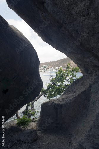 A view of a sea, motorboat and a tree through the rock formation in the island of Patmos, Greece in summer time.