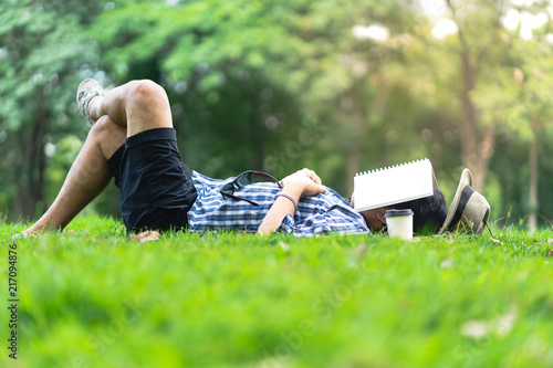 mature man sleeping on green grass in city park  with a book covers on face