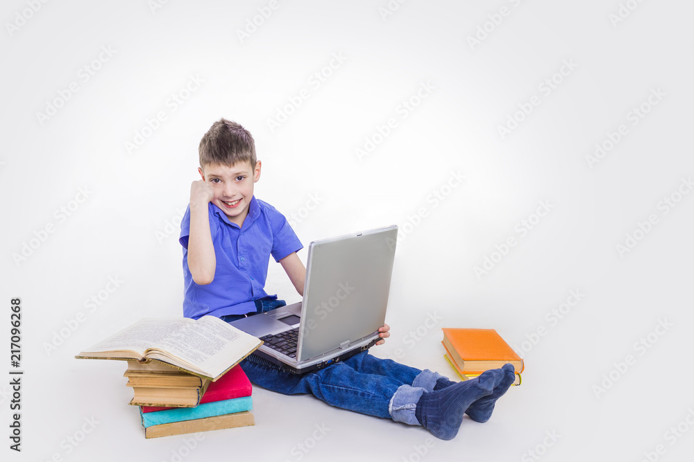 Portrait of cute teen schoolboy sitting near books and typing on laptop keyboard. Happy and surprised little boy, caucasian model isolated on white studio background. Education, study, studying Portrait of cute teen schoolboy sitting near books and typing on laptop keyboard. Happy and surprised little boy, caucasian model isolated on white studio background. Education, study, studying