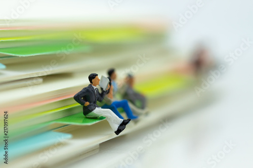 Miniature people: Businessman reading newspaper with big book. Image use for business, education concept.