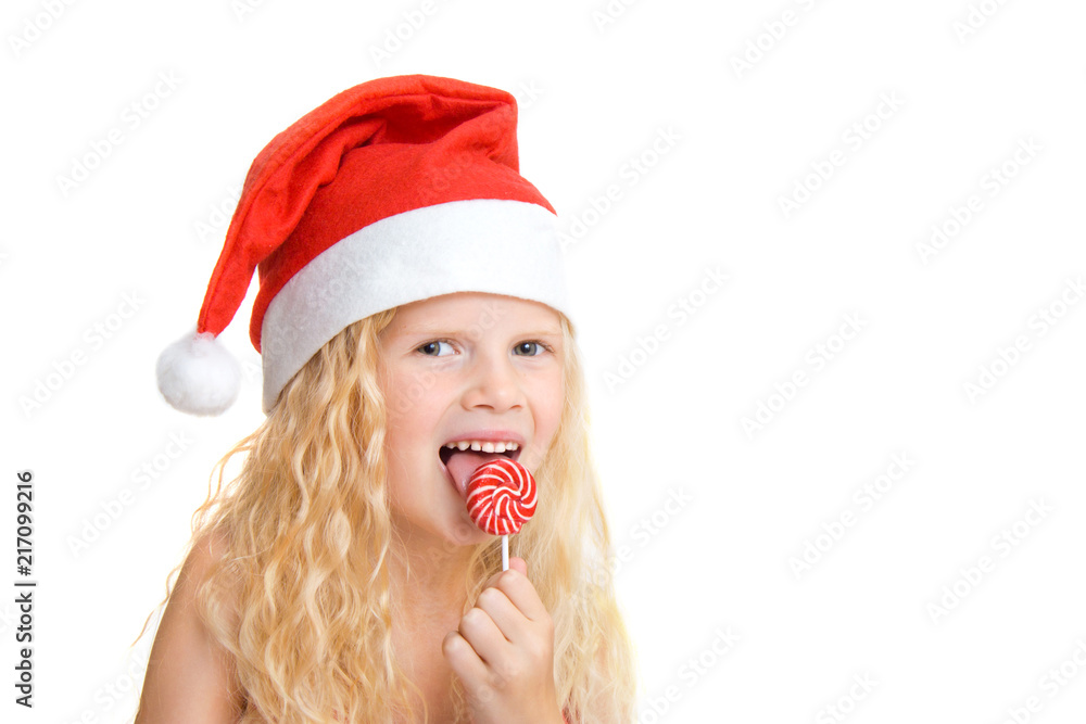 Christmas and new year card with cute little blonde girl in red santa claus hat with lollipop looking at camera close-up isolated on white. Copyspace - holidays, winter and celebration concept Christmas and new year card with cute little blonde girl in red santa claus hat with lollipop looking at camera close-up isolated on white. Copyspace - holidays, winter and celebration concept