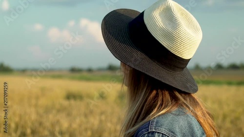 In this slow motion portrait shot you can see young beautiful woman standing in front of huge summer wheat field and looking into the horizon sky with clouds. photo