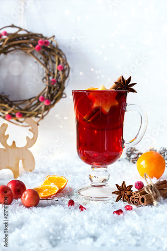 Christmas mulled wine with oranges and spices on white snow background.