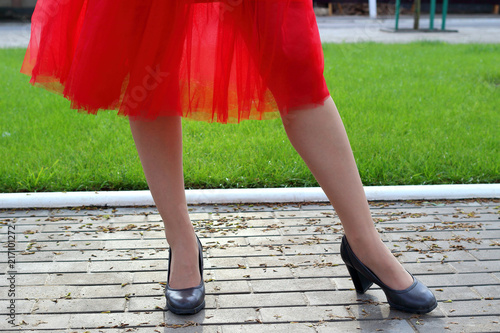 Legs of a girl in a red skirt pack and shoes in the sun