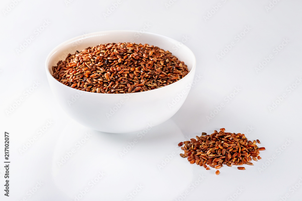 Bowl of red raw rice and a pile of rice isolated at white background. Bowl of red raw rice and a pile of rice isolated at white background.