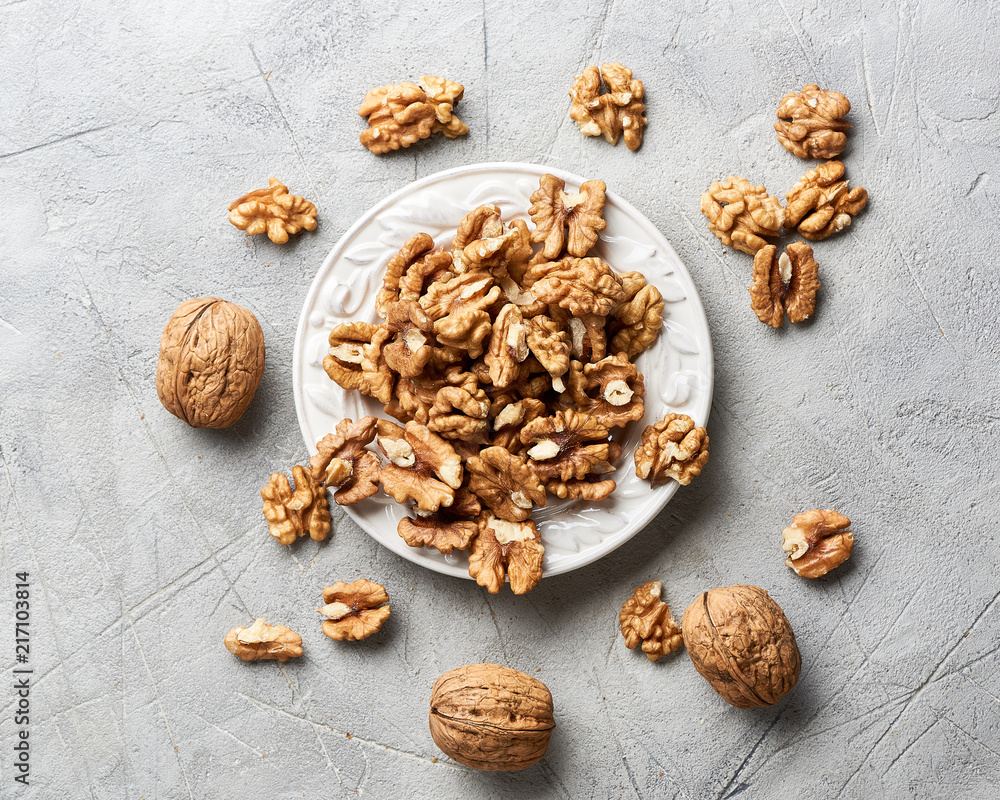 Walnut kernels on white plate over gray background. Walnut kernels on white plate over gray background.