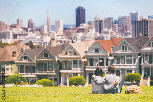 San Francisco - Alamo Square people. Couple tourists relaxing in Alamo Park by the Painted Ladies houses iconic landscape, The Seven Sisters, San Francisco, California, USA.