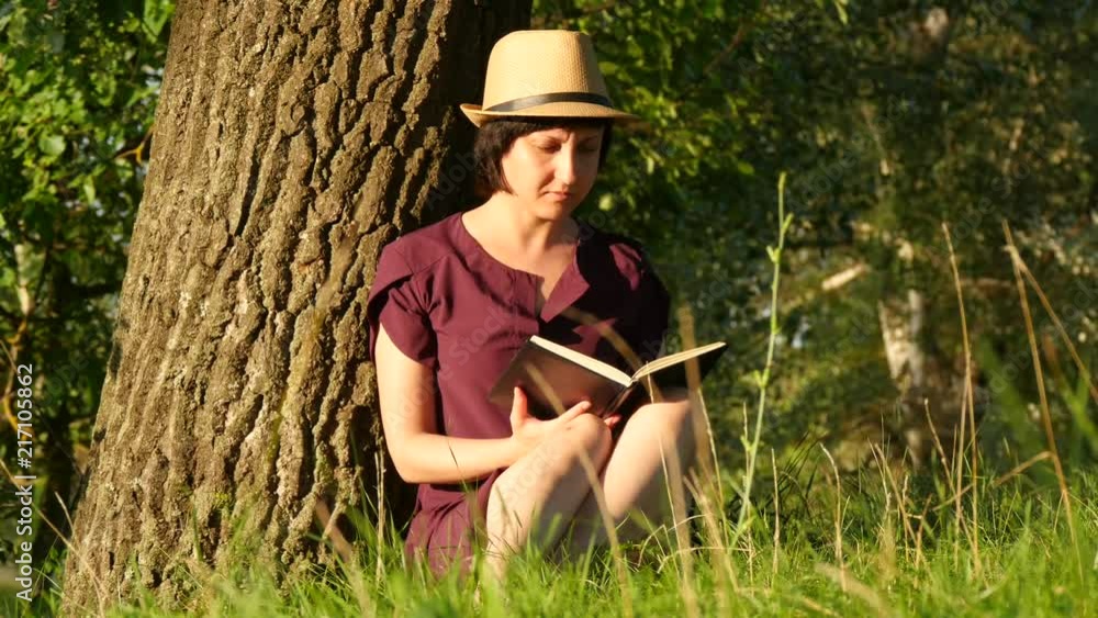 Young female student reading a book in the Park. Culture, reading, education. Girl sitting by the tree. Camera movement. Young female student reading a book in the Park. Culture, reading, education. Girl sitting by the tree. Camera movement.
