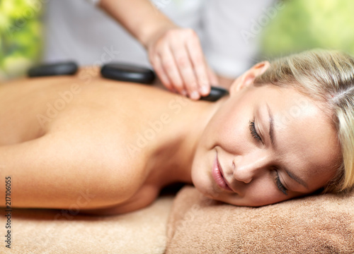 beauty, wellness and relaxation concept - close up of beautiful young woman having hot stone massage in spa over green natural background