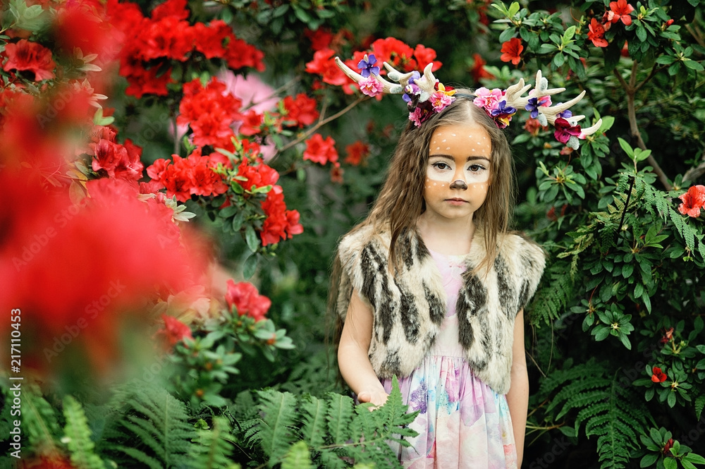 Fairy tale girl. Portrait a little girl in a deer dress with a painted face in the forest. Big antler. Fantasy girl. Springtime. Fairy tale girl. Portrait a little girl in a deer dress with a painted face in the forest. Big antler. Fantasy girl. Springtime.