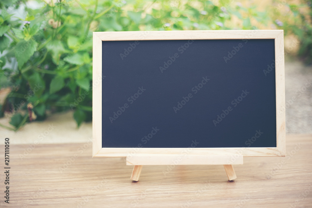  Black board on wood table top with sun and blur green tree bokeh background, Template mock up for display of product