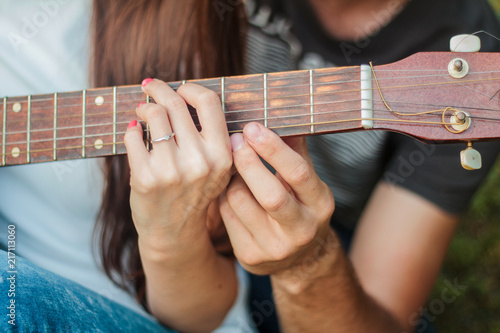 Obraz na płótnie hands of a guy and a girl on a guitar fretboard, learns to play the guitar on the lawn in the park w salonie