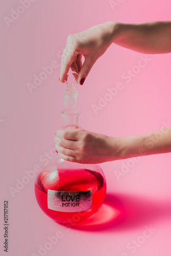 cropped shot of woman opening flask with red colored love potion on pink surface