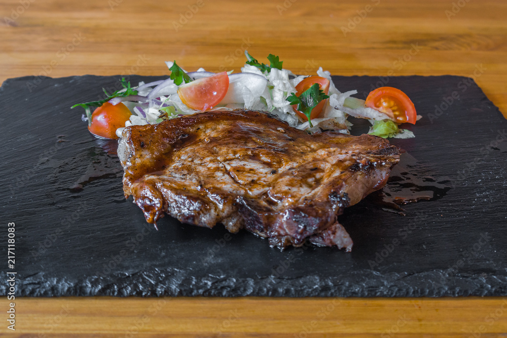 meat with vegetables on a stone board. tomatoes. and spices, a delicious dish
