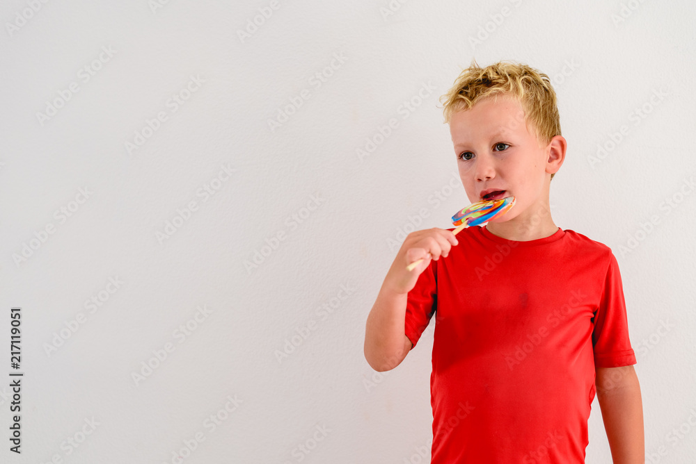 Boy with red shirt on white background eating a lollipop colorful fun and laughing. Boy with red shirt on white background eating a lollipop colorful fun and laughing.