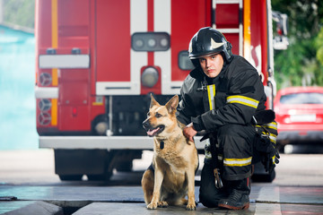 Photo of young fireman squatting next to service dog near fire engine