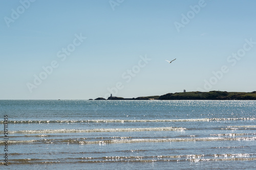 Harsh sunlight reflection on sea waves and Llanddwyn Island in the background on middy in hot summer