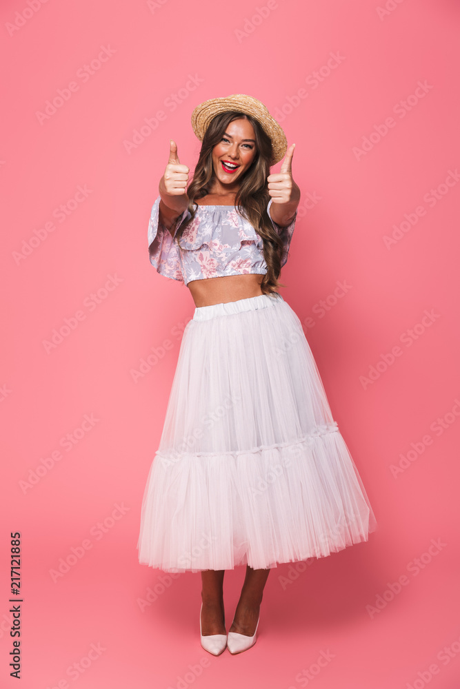Full length portrait of beautiful excited woman 20s wearing straw hat and fluffy skirt showing thumbs up, isolated over pink background in studio Full length portrait of beautiful excited woman 20s wearing straw hat and fluffy skirt showing thumbs up, isolated over pink background in studio