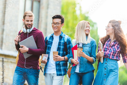 portrait of smiling multiethnic students with backpacks walking in park